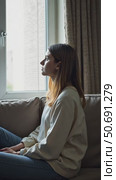 Side view young woman looking away at window sitting on couch at home. Frustrated confused female feels unhappy problem in personal life quarrel break up with boyfriend or unexpected news. Стоковое AI-видео, аниматор Sergey Grishin / Фотобанк Лори