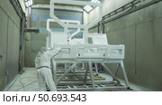 Person in a protective suit applying paint to a large automotive frame component in a manufacturing facility. Стоковое видео, видеограф Дмитрий Нечаев / Фотобанк Лори