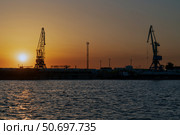 Astrakhan, Russia, 05.04.2025: Port cranes for cargo transshipment on the mooring line of the Astrakhan port on the right bank of the Volga River against the background of the setting sun. Редакционное фото, фотограф Ula Ulachka / Фотобанк Лори