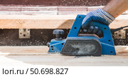 A hand-held electric planer in the hands of a craftsman. A man planing boards with an electric tool. Production of wooden products. Construction, wood processing. Стоковое фото, фотограф Photojuli / Фотобанк Лори