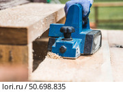 A hand-held electric planer in the hands of a craftsman. A man planing boards with an electric tool. Production of wooden products. Construction, wood processing. Стоковое фото, фотограф Photojuli / Фотобанк Лори