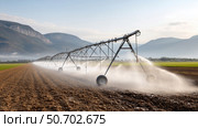 Irrigation system watering a large agricultural field in a sunny landscape. Ирригационная система, поливающая большое сельскохозяйственное поле в солнечном ландшафте. Стоковое AI-изображение, AI-художник Katsiaryna Repich / Фотобанк Лори
