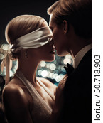 Romantic cover. A dominant billionaire whispers something in a woman's ear, blindfolding her with a silk ribbon, against the background of the lights of a big city. Стоковое AI-изображение, AI-художник Корчагина Анастасия / Фотобанк Лори
