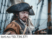 Serious pirate captain posing on a sailing ship wearing tricorn hat. Стоковое AI-изображение, AI-художник Иван Рябоконь / Фотобанк Лори