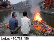 Two men observing cremation ceremony on bagmati river in kathmandu. Стоковое AI-изображение, AI-художник Юрий Поздников / Фотобанк Лори