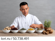 Asian herbalist preparing traditional chinese medicine with herbs and roots. Стоковое AI-изображение, AI-художник Юрий Поздников / Фотобанк Лори