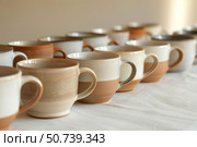 Handmade ceramic mugs displayed on table in pottery workshop. Стоковое AI-изображение, AI-художник Иван Рябоконь / Фотобанк Лори
