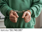 Hands of individual in green sweatshirt are handcuffed together, symbolizing restraint and confinement. Стоковое AI-изображение, AI-художник Гайфуллина Дина / Фотобанк Лори