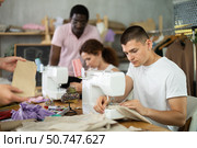 Young man stitching at machine during sewing class for adults. Стоковое фото, фотограф Яков Филимонов / Фотобанк Лори