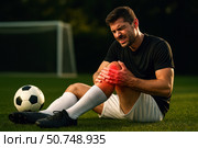 Injury on the Field: A Soccer Player Clutches His Knee in Pain After Sustaining an Injury During an Intense Match on a Lush Green Pitch. Стоковое AI-изображение, AI-художник Башкирова Анна / Фотобанк Лори