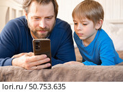 Father and son little boy laughing and using phone. They watching funny videos together, playing games on smartphone. Concept technology, smart phone addicted. Fun weekend activity. Modern fatherhood. Стоковое фото, фотограф Марина Демидюк / Фотобанк Лори