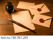 Vintage still life with blank old paper, fountain pen, inkwell, and envelopes with wax seals on rustic wooden table. Стоковое AI-изображение, AI-художник Павел Муравьев / Фотобанк Лори