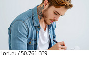 Focused man with neck tattoo drawing on paper, creative artist in denim jacket sketching design, close up portrait of illustrator at work indoors. Стоковое AI-изображение, AI-художник Павел Муравьев / Фотобанк Лори