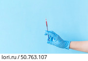 Human hand wear blue nitrile disposable glove holding syringe above light blue background. Safety first and vaccination concept. Стоковое фото, фотограф Акимова Надежда / Фотобанк Лори