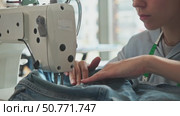 tailor is stitching denim with sewing machine, concentrating on process. Hands carefully guide fabric under needle. Стоковое видео, видеограф Strunov David / Фотобанк Лори