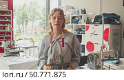 young, lovely dressmaker, standing in her workshop. She is surrounded by sewing tools and has measuring tape around her neck. Стоковое видео, видеограф Strunov David / Фотобанк Лори
