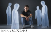 Young man feeling excluded, sitting alone with ghostly figures. Стоковое AI-видео, аниматор Юрий Поздников / Фотобанк Лори
