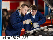Two auto mechanics checking engine oil level under the hood of car together in garage. Стоковое фото, фотограф Яков Филимонов / Фотобанк Лори