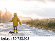 A boy in yellow rubber boots and a raincoat runs through puddles, having fun and playing with a remote-controlled car after it rains. Summer and autumn holidays. A happy childhood. Стоковое фото, фотограф Photojuli / Фотобанк Лори