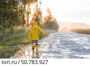 A boy in yellow rubber boots and a raincoat runs through puddles, having fun and playing after it rains. Summer and autumn holidays. A happy childhood. Стоковое фото, фотограф Photojuli / Фотобанк Лори
