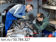 Two auto mechanics disassemble a car engine together for repair in garage. Стоковое фото, фотограф Яков Филимонов / Фотобанк Лори