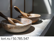 Two wooden bowls overflowing with white bath salts are casting shadows on a marble shelf. Стоковое AI-изображение, AI-художник Иван Рябоконь / Фотобанк Лори