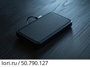 External hard drive charging on dark wooden table. Стоковое AI-изображение, AI-художник Иван Рябоконь / Фотобанк Лори
