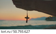 Silhouette of praying hands holding a cross pendant in front of sea sunset with mountains in the distance. Стоковое видео, видеограф Igor Tichonow / Фотобанк Лори