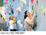 Motivated young girl climbing without ropes and harnesses on artificial bouldering wall in fitness center. Стоковое фото, фотограф Яков Филимонов / Фотобанк Лори