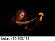 An ominous witch with long curly hair holds a magical fire. Tongues of flame on the palms of a red-haired smirking woman. Witchcraft. Стоковое фото, фотограф Михаил Решетников / Фотобанк Лори