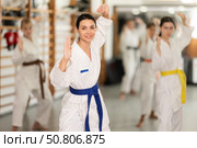 Positive young woman practicing kata standing in row with others. Стоковое фото, фотограф Яков Филимонов / Фотобанк Лори
