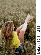 Young woman relaxes in a wheat field during golden hour, stretching legs and enjoying nature's tranquility. Стоковое фото, фотограф Вербицкая Светлана / Фотобанк Лори