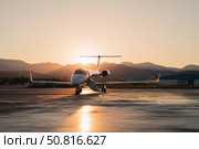 Luxury private jet parked on a glowing runway with mountain silhouette and soft sunset light, ideal for aviation and elite travel concepts. Стоковое AI-изображение, AI-художник Александра Троицкая / Фотобанк Лори