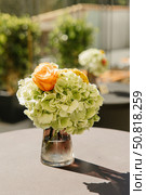A beautifully arranged floral centerpiece featuring vibrant orange roses and delicate green hydrangeas in a glass vase, perfect for enhancing any elegant setting. Стоковое фото, фотограф Башкирова Анна / Фотобанк Лори