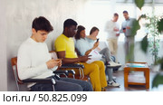 Relaxed young guy browsing websites on smartphone while sitting in lobby of job center or employment office, waiting for interview or conversation with career counselor. Стоковое видео, видеограф Яков Филимонов / Фотобанк Лори