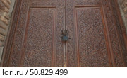 Traditional hand-carved wooden door with detailed flora, geometric ornaments in Islamic style architecture, locked with a padlock, embedded in an ancient brick wall in historical Samarkand, Uzbekistan. Стоковое видео, видеограф Сергей Тимофеев / Фотобанк Лори