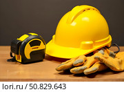 On the table are yellow work helmet, a tape measure, and construction gloves. Стоковое AI-изображение, AI-художник Галина Эмберг / Фотобанк Лори