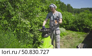 Man in Headphones Using Garden Branch Shredder on Sunny Summer Day, Wearing Overalls, Loading Sticks with Pusher Tool, Gardening, Recycling Yard Waste, Eco-Friendly Work Yard ESG, recycling process. Стоковое видео, видеограф Сергей Тимофеев / Фотобанк Лори