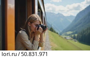 Beautiful happy young woman hangs out of train open window and make photo on vintage analog camera. Travel and explore more wanderlust concept. Female touristing mountains. Стоковое AI-видео, аниматор Sergey Grishin / Фотобанк Лори