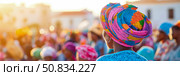 Cultural Gathering: Woman with vibrant head wrap amid a joyful crowd, celebrating unity and diversity in a bright, sunlit setting. Стоковое AI-изображение, AI-художник Данила Большаков / Фотобанк Лори