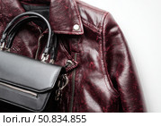 Maroon leather jacket with zippers and pockets and black leather stylish bag. Modern outerwear. Close-up. Fashion background. Autumn urban street clothes. Fashionable concept. Women's casual outfit. Стоковое AI-изображение, AI-художник Марина Демидюк / Фотобанк Лори