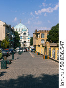Yevpatoria, Russian Federation - July 05, 2025: Scenic street view with cobblestone pavement leading to a beautiful blue-domed church under a clear sky in a vibrant urban setting. Редакционное фото, фотограф Ирина Ручушкина / Фотобанк Лори