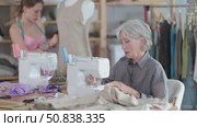 Skillful mature tailoress using sewing-machine while young girl working with mannequin in sewing workshop. Стоковое видео, видеограф Яков Филимонов / Фотобанк Лори