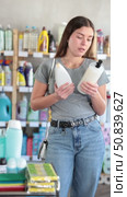 Smiling casual young woman in household goods store thoughtfully examining shampoo bottles, carefully reading product labels while deciding on best option. Стоковое видео, видеограф Яков Филимонов / Фотобанк Лори