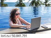 Young freelancer traveler woman working remotely on computer at pool in luxury resort during her summer holiday. Work from anywhere, Technology and lifestyle concept, copy space. High quality photo. Стоковое фото, фотограф Ирина Михайличенко / Фотобанк Лори