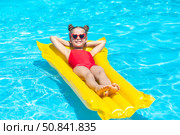 Happy little girl in red swimsuit lies comfortably on yellow inflatable mattress in swimming pool with blue water on warm summer day on tropical vacation. Relaxation, fun, carefree childhood concept. Стоковое фото, фотограф Ирина Михайличенко / Фотобанк Лори