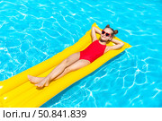 Top view little girl in red swimsuit lies comfortably on yellow inflatable mattress in swimming pool with blue water on summer day on tropical vacation. Relaxation, fun, carefree childhood concept. Стоковое фото, фотограф Ирина Михайличенко / Фотобанк Лори