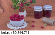Summer rural still life with ripe freshly picked raspberries in bowl, jars of homemade jam and bouquet of raspberry branches with berries on wooden garden table on July day. Video of organic  berries. Стоковое видео, видеограф Виктория Катьянова / Фотобанк Лори