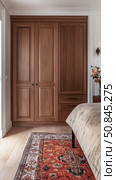 Elegant wooden wardrobe and cozy bedroom interior with patterned rug. Стоковое AI-изображение, AI-художник Катерина Бондарец / Фотобанк Лори