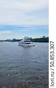 On a sunny day, a white yacht sails along a wide river, against which city buildings and a green coastline are visible. Summer yacht trip. Holidays on the water. Стоковое фото, фотограф Анна Чижова / Фотобанк Лори